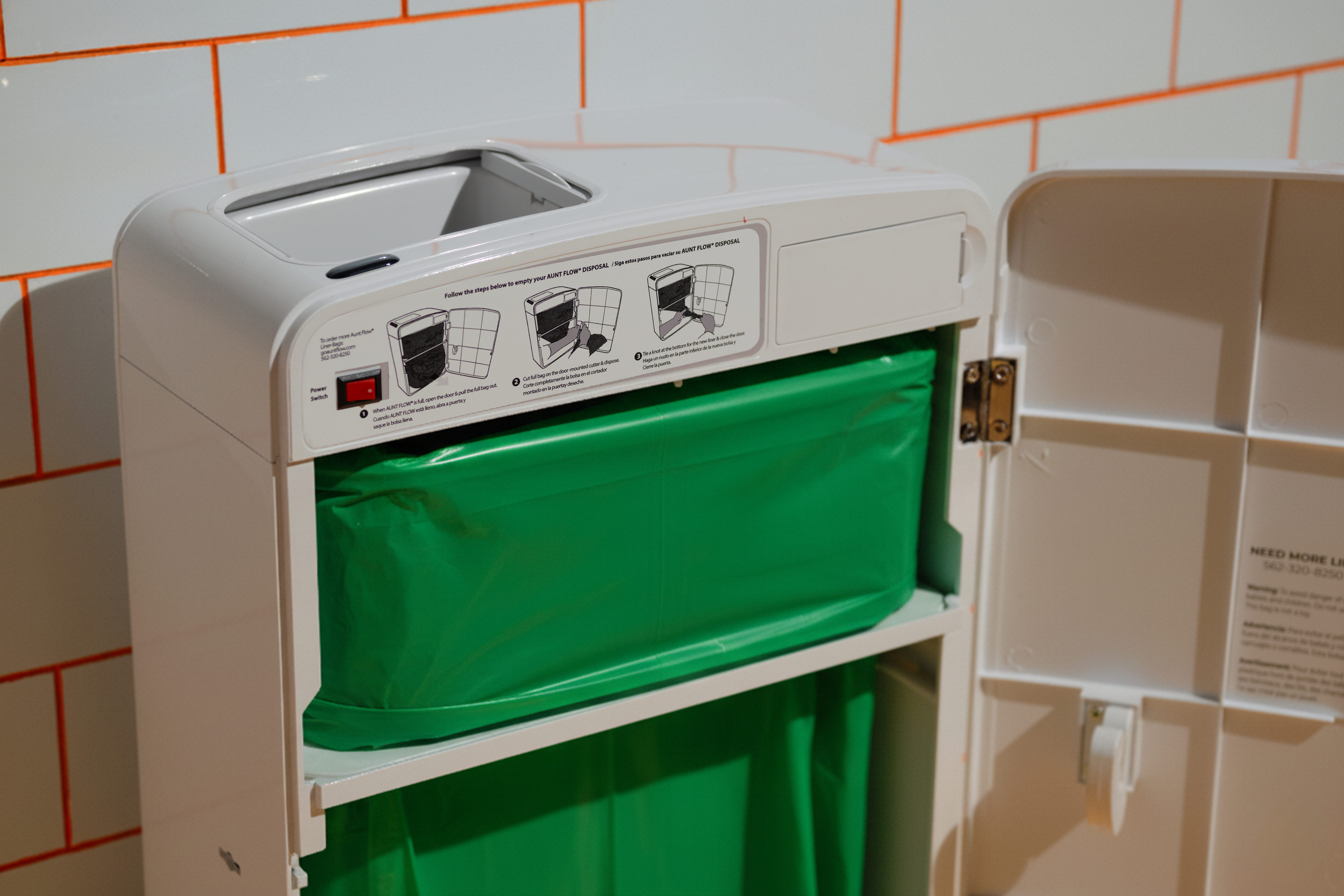 White appliance with green bag inside against a tiled wall background