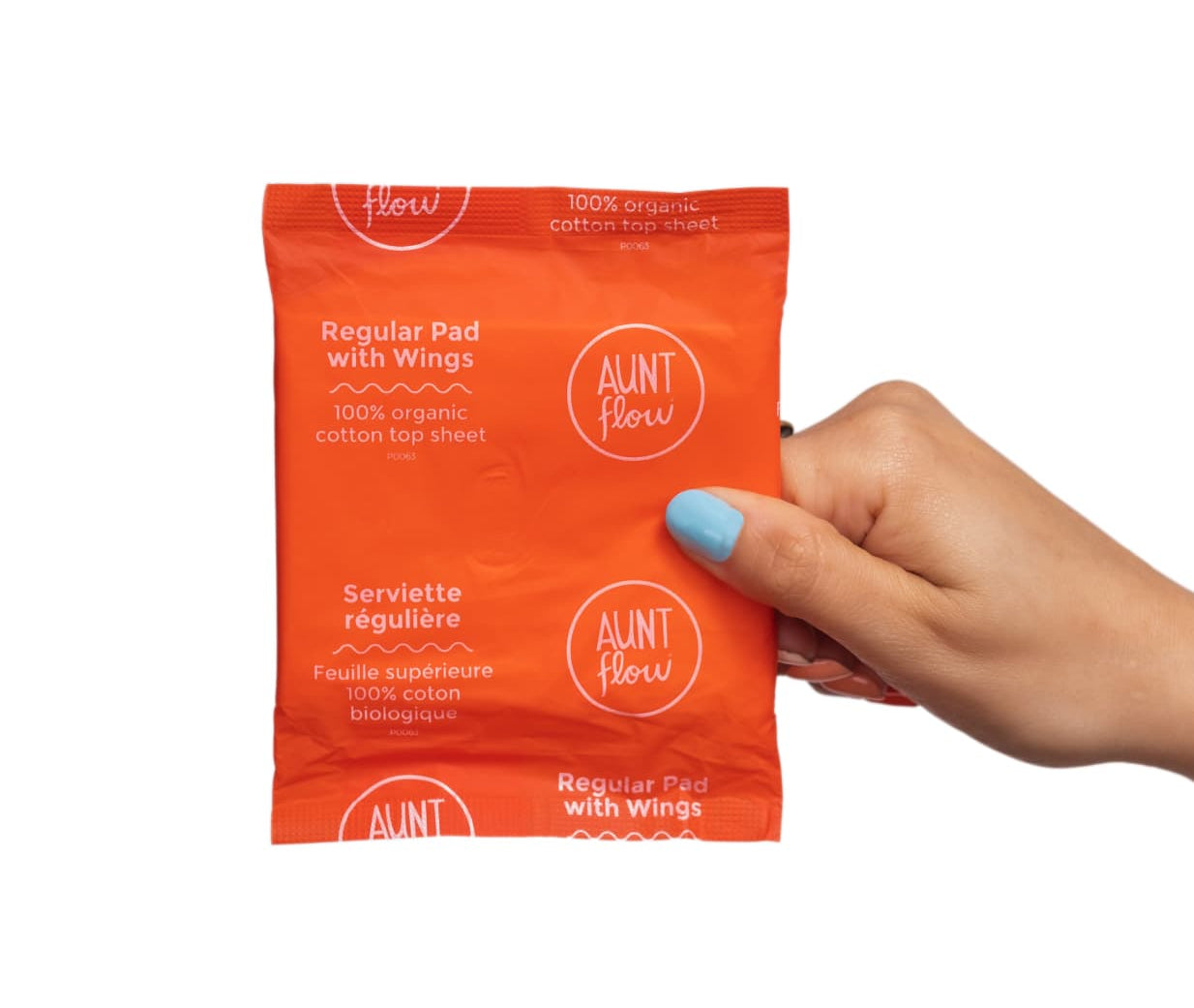 An orange Aunt Flow Regular Pad with Wings product pouch held by a hand with light blue nail polish against a plain white background.