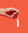 Hand holding unwrapped applicator tampon against coral background
